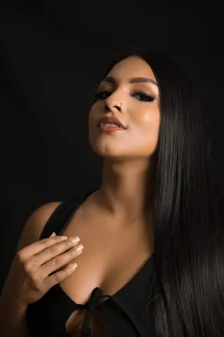Portrait of a beautiful woman with long dark hair wearing a black top against a dark moody background.