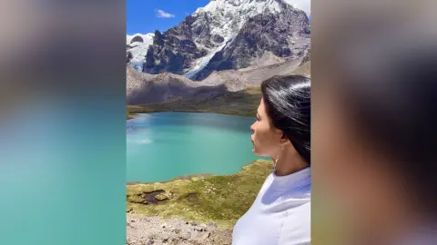Side profile of a woman in a white top looking at a turquoise mountain lake under snowy peaks.