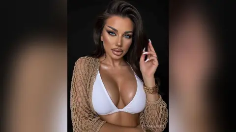 Glamorous woman in a white bikini and beige crochet cover-up posing with elegant makeup against a dark background.