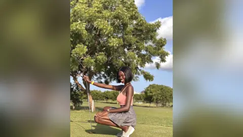 Smiling young woman in a pink tank top and grey skirt playing golf outdoors on a sunny day.