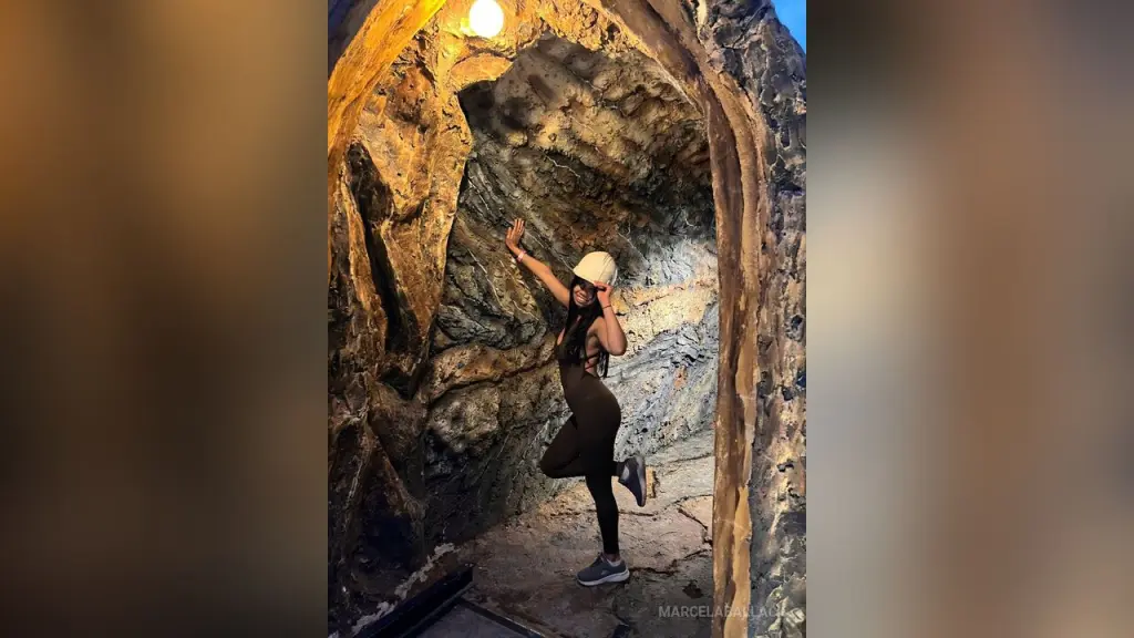 MarcelaBallack — Adventurous woman in black activewear posing inside a dark, textured rocky cave with dramatic lighting.