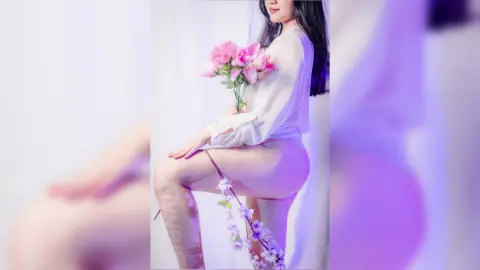 Young woman in a white blouse holding pink flowers in a soft, dreamy aesthetic setting.