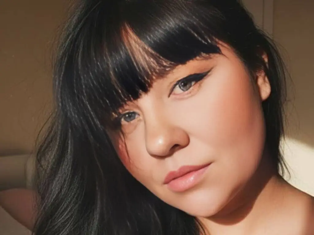 Close-up portrait of a woman with dark hair and winged eyeliner in warm, natural sunlight.