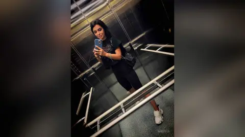 Young woman in black casual outfit taking a mirror selfie in a modern elevator.