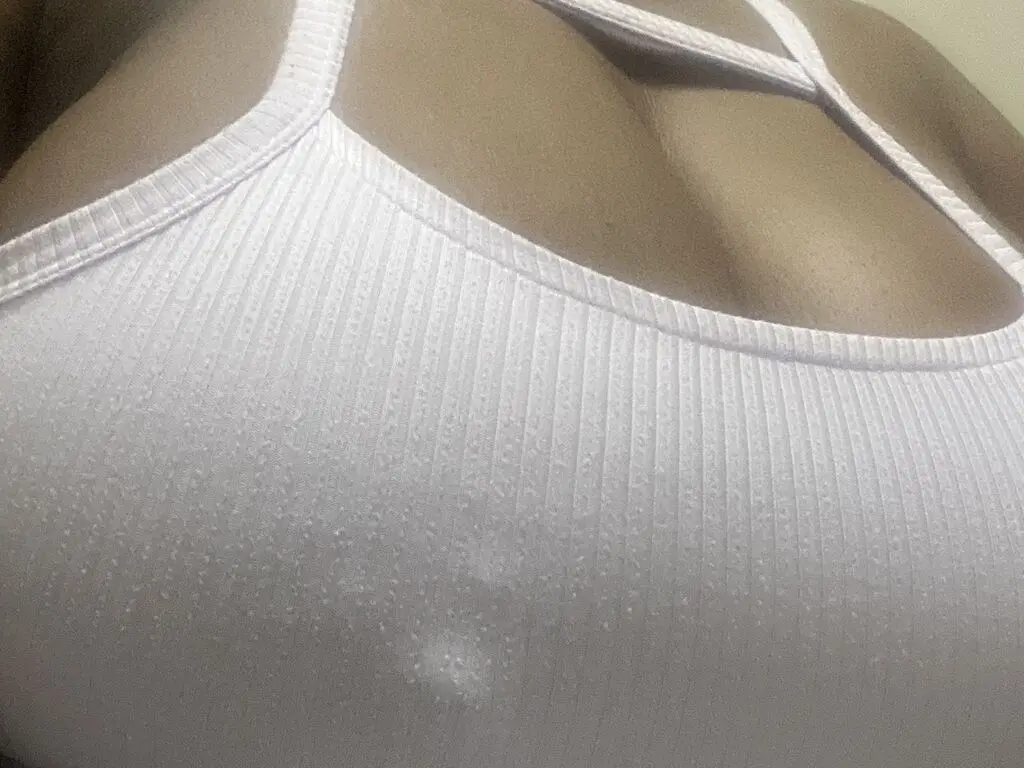 Close-up of a woman wearing a white ribbed cotton camisole tank top in soft natural lighting.