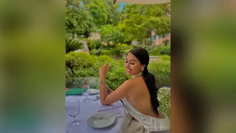 Smiling woman in a white strapless dress dining at an outdoor garden table on a sunny day.