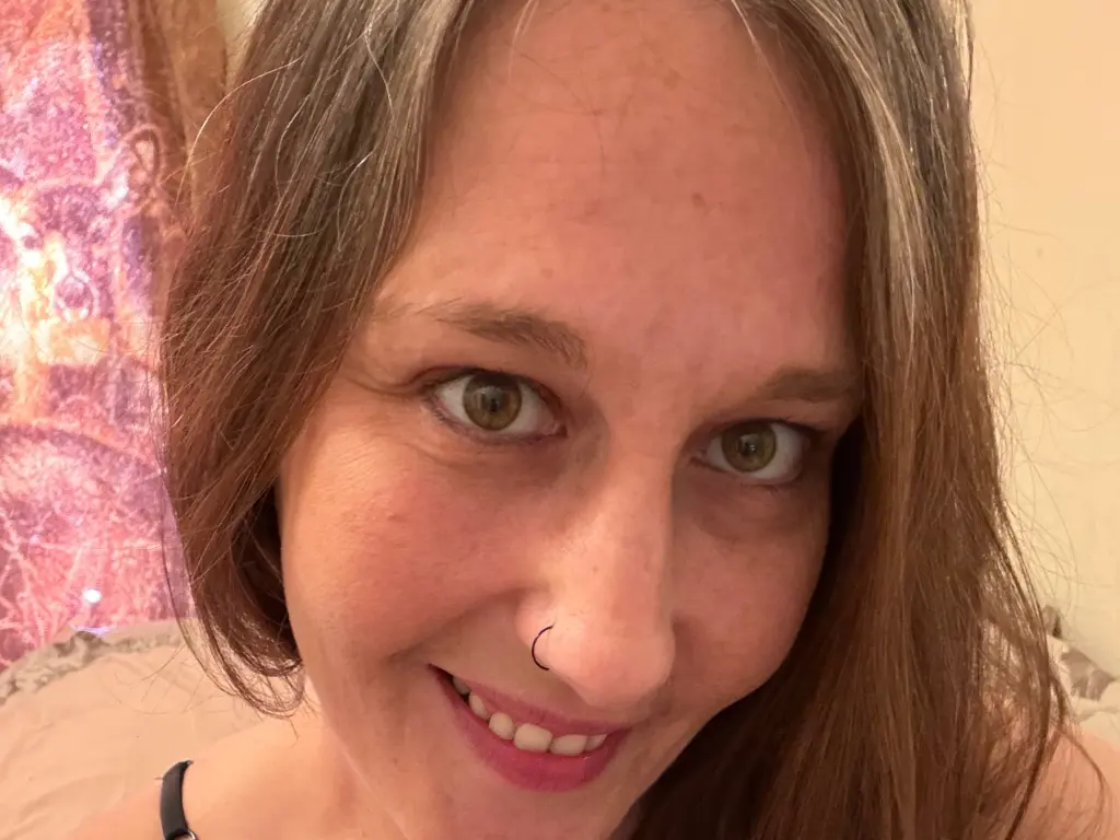 DirtyWife4Life looks directly at the camera with a smile, showing her face and long brown hair in a close-up shot.