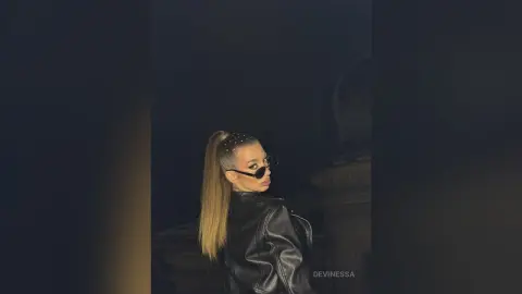 DeviNessa poses in a black leather jacket with her blonde hair in a high ponytail and dark sunglasses.