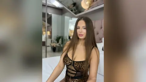 Young woman in a leopard print bodysuit relaxing in a bright, modern bedroom setting.