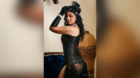 Elegant woman in black vintage corset and lace gloves posing glamorously in a classic indoor setting.