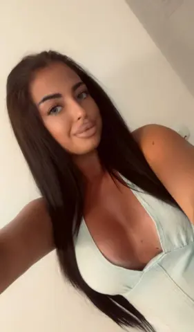 Young woman with long dark hair wearing a light mint green halter top in a bright indoor setting.