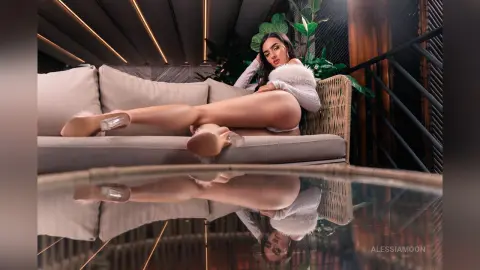 Elegant woman in a white fuzzy sweater lounging on a sofa in a moody, modern luxury interior.