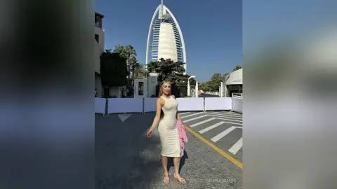 Stylish woman in a white sleeveless dress standing on a sunny street with the Burj Al Arab in the background.