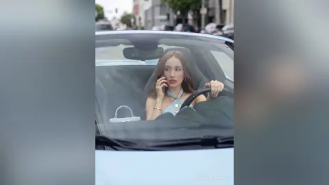 Stylish young woman in a light blue halter top driving a light blue convertible car on a city street.