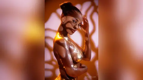 Glamorous woman in gold sequin attire posing under warm, artistic shadows in a moody studio setting.