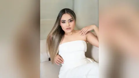 Elegant woman in a white strapless dress posing gracefully on a white sofa with a soft, dreamy mood.