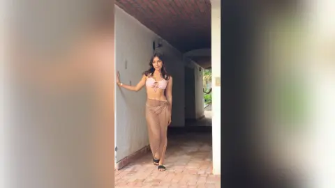Young woman in a pink bikini top and mesh skirt posing in a sunlit Mediterranean villa hallway.