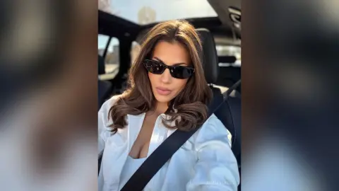 Stylish woman in a white shirt and sunglasses sitting in a car on a sunny day.