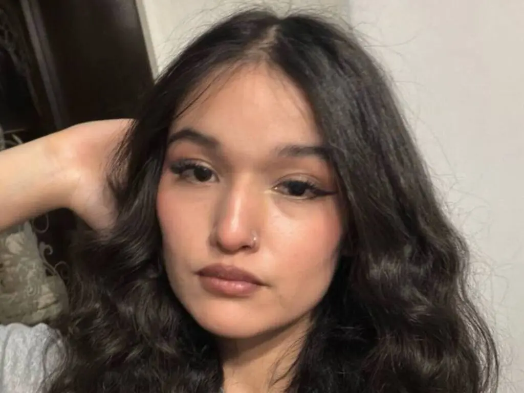 SorayaBenezra poses with her hand behind her head, showing off her long, wavy dark hair and winged eyeliner.