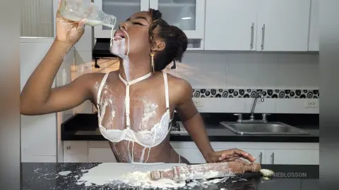 Young woman in white lace lingerie playfully covered in flour while baking in a modern kitchen.