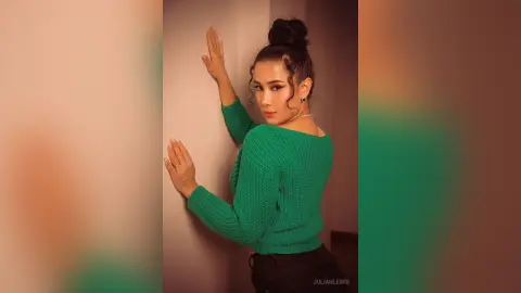 Elegant woman in a green knit sweater posing against a warm wall with a sophisticated mood.