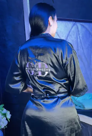 Woman in a black satin Grupo Derroche robe relaxing in a moody, blue-lit room.