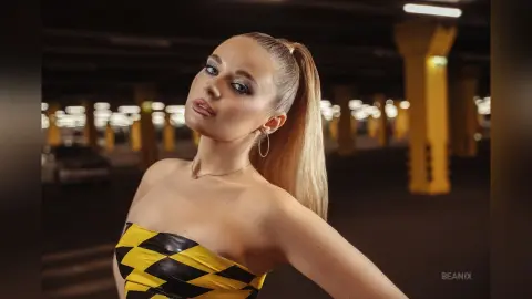 BeaNix poses in a yellow and black patterned tube top with her blonde hair in a high ponytail.