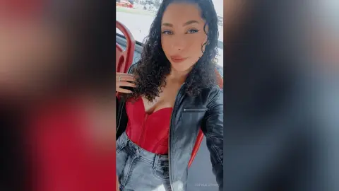 Smiling woman in a red corset and black leather jacket sitting in a car for a stylish portrait.