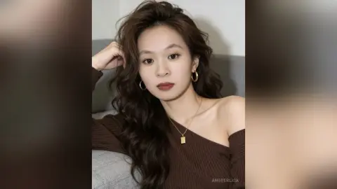 Young woman with wavy brown hair wearing a brown ribbed off-the-shoulder top and gold jewelry in a soft mood.