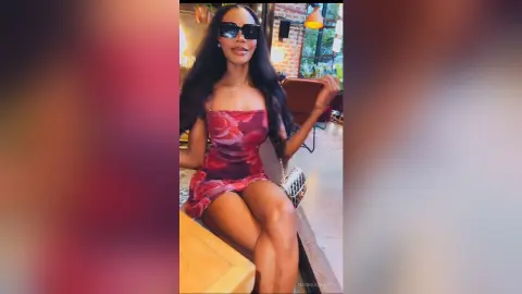 Stylish woman in a red floral mini dress and sunglasses sitting in a modern cafe setting.