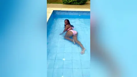 KattyLeya — KattyLeya smiles while floating on her back in a blue swimming pool wearing a pink bikini.