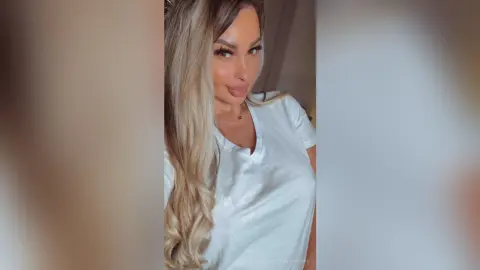 Smiling blonde woman in a casual white t-shirt posing for a bright indoor selfie.