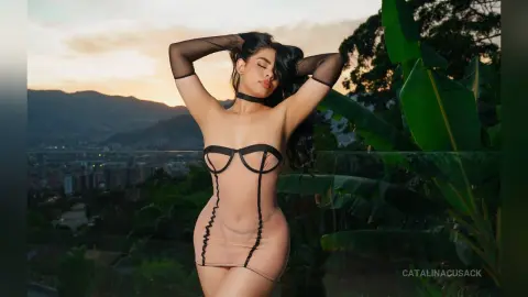 Elegant woman in a sheer nude bodysuit posing against a scenic mountain sunset backdrop.