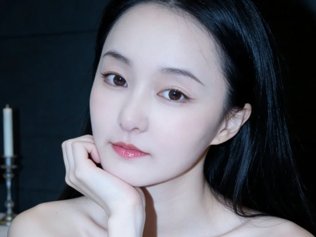 JiangHuihui — JiangHuihui poses with her chin resting on her hand, looking at the camera with long black hair and a dark background.