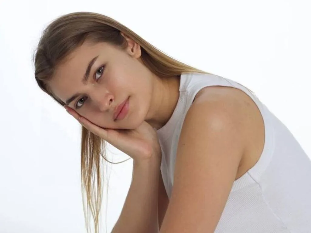 ElizSautner rests her chin on her hand, looking forward with long blonde hair against a white background.