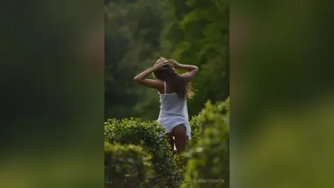 Dreamy portrait of a woman in a white summer dress standing in a lush green garden at sunset.