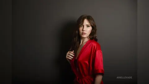 Elegant woman in a red silk robe posing against a dark moody background.