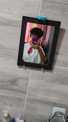 Young woman with curly hair in a white shirt and red bandana taking a mirror selfie in a modern bathroom.