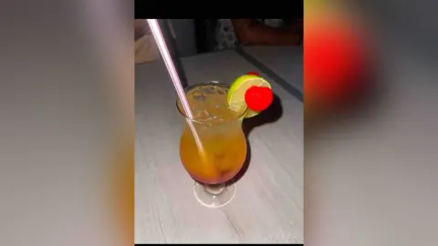 KattyLeya — KattyLeya enjoys a tropical cocktail with a lime slice and a red cherry on a table.