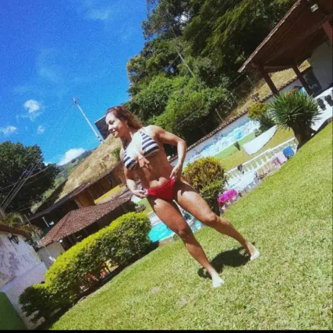 Smiling woman in a striped bikini relaxing on a sunny green lawn near a tropical villa and pool.