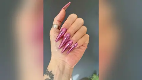 Close-up of long metallic pink stiletto nails on a hand with a silver ring for trendy manicure inspiration.