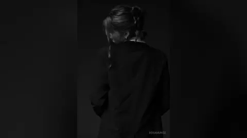 Moody black and white portrait of a woman in a dark shirt looking away in a shadowy setting.