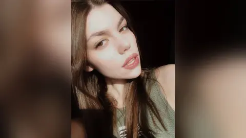 Close-up portrait of a young woman with long brown hair wearing a green ribbed tank top in soft natural lighting.