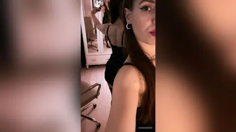 Young woman in a black sleeveless top taking a mirror selfie in a brightly lit room.