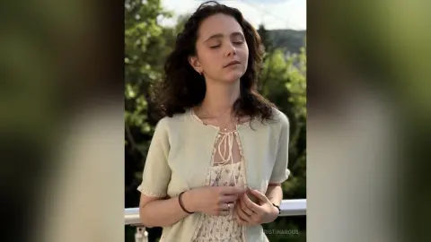 Young woman in a light green cardigan and floral dress relaxing outdoors in soft natural sunlight.