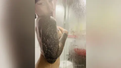 Tattooed woman in a steamy bathroom setting with a moody, intimate atmosphere.