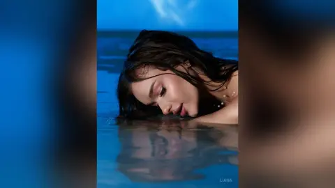 Beautiful woman with wet hair relaxing in blue ocean water at twilight for a serene moody portrait.
