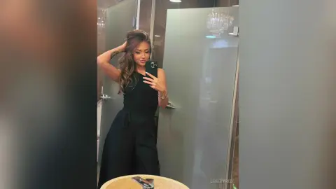 LesleyRed takes a mirror selfie wearing a black sleeveless jumpsuit in a modern bathroom.