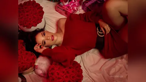 Glamorous woman in a red dress lying among red roses and gifts for a romantic Valentine's Day mood.