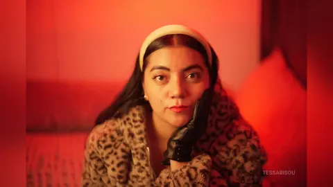 Woman in leopard print coat and black gloves posing under warm red lighting for a moody portrait.